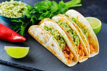 Tacos with fried minced meat and guacamole sauce on a dark background. Mexican tacos and...
