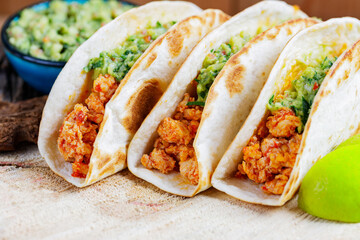 Mexican tacos with fried minced chicken and guacamole sauce on a wooden boards. Tacos, guacamole and lime on wooden background. Mexican cuisine
