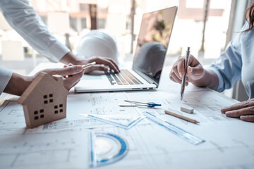 Architects or engineering team consulting and analyzing working on objects tools and construction drawings inspection planning new architectural project on blueprint and model house in modern office