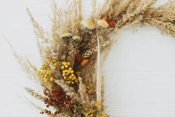 Creative boho wreath with dried pampas grass, tansy wildflowers, wheat, dog-rose berries on white...
