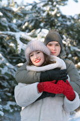 Young couple in love hugs against snow-covered trees background. Vertical frame