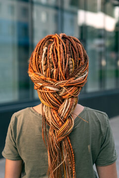 Beautiful girl with a long braid of red dreadlocks. The girl stands with her back to the camera. Close-up.
