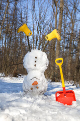 funny cheerful snowman in yellow boots stands upside down in a snowy forest. Vacation during the...