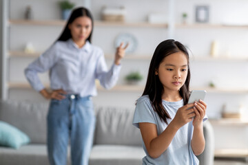 Asian mother and daughter quarreling because of overuse the smartphone, girl not paying attention to her mom