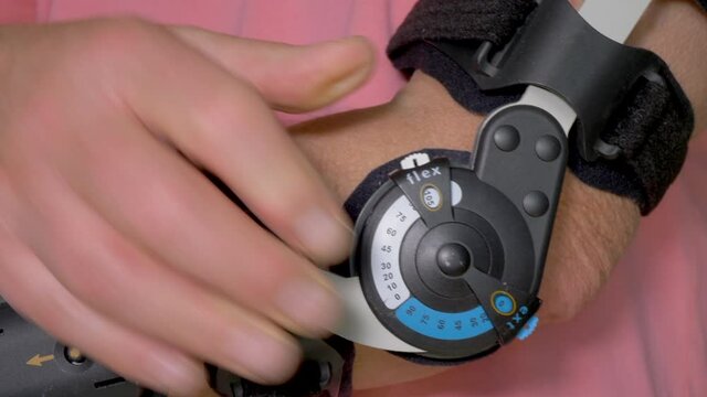Closeup POV shot of an elderly man adjusting a fitted arm brace, for a greater range / degree of elbow movement.