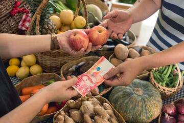 A man hands over a 50 peso bill to pay for two apples. Buying fruits at a small market stall.