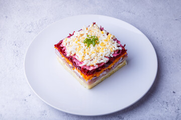 Herring salad under a fur coat. Traditional Russian multilayered salad from herring, beets, potatoes, carrots and eggs. Close-up, grey background.