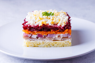 Herring salad under a fur coat. Traditional Russian multilayered salad from herring, beets, potatoes, carrots and eggs. Close-up, grey background.