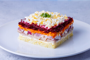Herring salad under a fur coat. Traditional Russian multilayered salad from herring, beets, potatoes, carrots and eggs. Close-up, grey background.