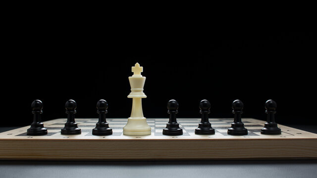 White chess king surrounded by black pawns. Chess pieces are hardly on the board. On black background.