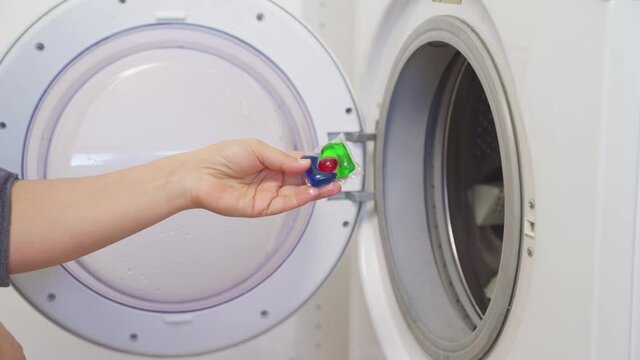 a woman puts capsule with laundry detergent in the washing machine. 