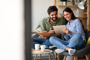 Free time together. Happy couple is spending weekend together at home. Reading book, tablet.