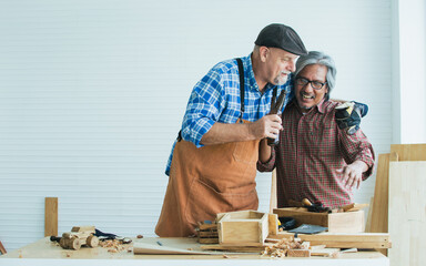 Two senior mixed race happy old male woodworkers wearing check shirts, drinking and holding bottle of beer to celebrate after work, successful creating DIY wooden furniture. Hobby, Retirement Concept.