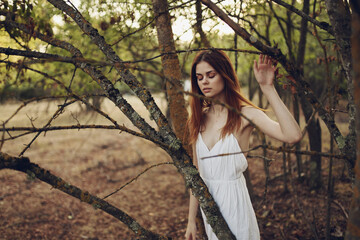 red-haired Woman in a white dress in the forest trees fallen leaves