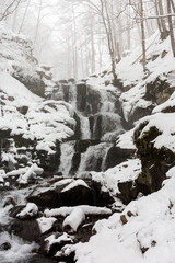 Fototapeta na wymiar Snowfall over mountain waterfall