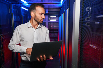 Bearded confident maintenance engineer in white shirt is working in database center