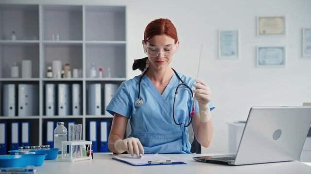 young female doctor with little rat on his shoulders holds a test tube with reagent in his hands and writes order on form while sitting in medical office