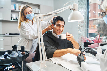 Cheerful male with coffee getting haircut and nail polishing