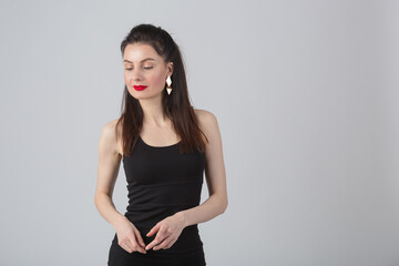 Young woman wearing little black dress, makeup and red lipstick posing in studio while looking away