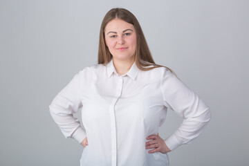 Plus size woman in white shirt. Happy female office worker posing in studio with friendly smile and hands on hips