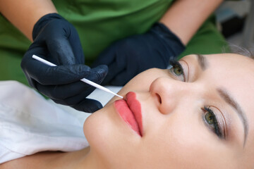 Young woman having permanent makeup on her lips at the beautician salon.