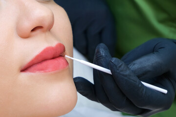 Young woman having permanent makeup on her lips at the beautician salon.