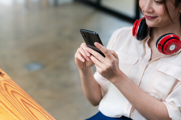 Image of a smiling young Asian woman wearing headphones holding a smartphone sitting in an office chair.