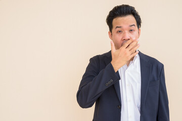 Portrait of Asian businessman wearing suit against plain background while looking shocked