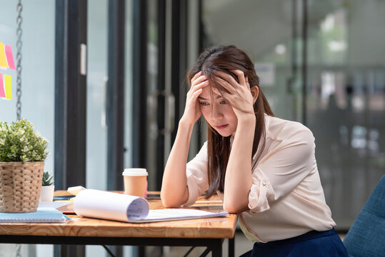 Young Asian businesswoman hands on her head when feeling tired and stressed about working hard on paperwork at the office.