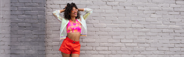cheerful african american woman in sunglasses posing near brick wall, banner