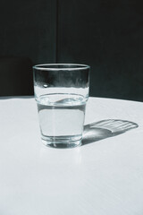glass with water with hard shadows on a white background. The concept of minimalism.