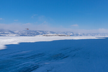 Snow-covered ice of Baikal in the Maloye More Strait near Olkhon Island against the background of mountains. Winter landscape on a sunny day. Natural background - 461060861