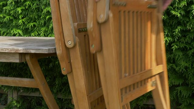 Closeup POV shot of a man&rsquo;s hands stacking four folded wooden garden / yard chairs against an old table, outside in the autumn sunshine.