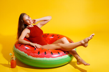 Full length smiling girl wears red swimsuit sits on inflatable ring isolated on yellow background