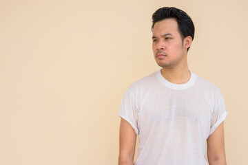 Portrait of Asian man wearing white t-shirt against plain background outdoors while thinking