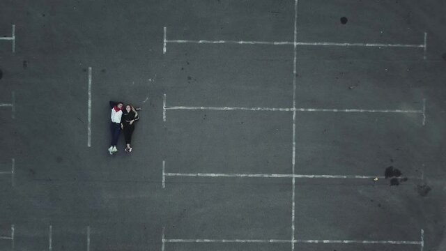 Young couple lying down on the shopping mall parking lot, drone shot from above
