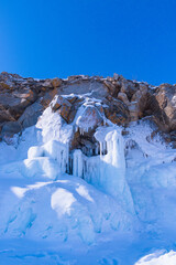 Blue ice waterfall on Ogoy Island in the Maloye More Strait on Lake Baikal on a sunny winter day. Siberia, Russia. - 461062272
