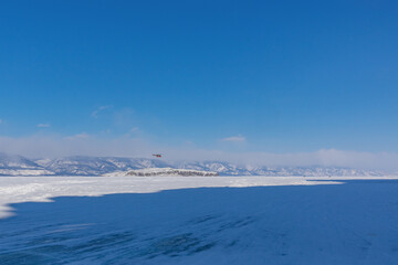 Snow-covered ice of Baikal in the Maloye More Strait near Olkhon Island against the background of mountains. Winter landscape on a sunny day. Natural background - 461062290