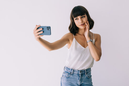 Portrait of a happy young woman taking pictures of herself over white background