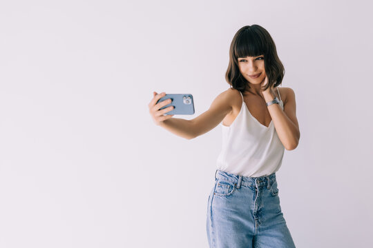 Portrait of a happy young woman taking pictures of herself over white background