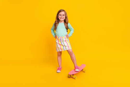 Full length photo of young little girl happy positive smile ride skateboard isolated over yellow color background