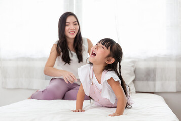 Obraz na płótnie Canvas Happy young Asian Mother and daughter enjoy on the bed near windows at home. Mom and little adorable spend time and laughing together at home.