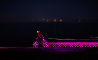 Bicycler riding along sea and leaving light trails at night 