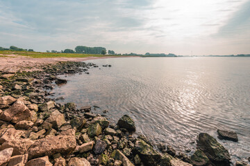 Stones and sand on the bank of the Dutch river Waal in the province of Gelderland near the small village of Herwijnen. It is still early in the morning of a beautiful autumn day.