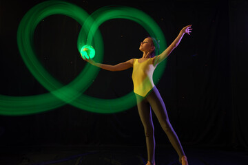 Girl gymnast doing exercise with shining ball in shape of earth with light painting effect