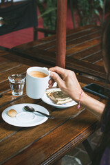 Woman holding cup of coffee with alfajor, sitting at a bar table, outdoors in the afternoon
