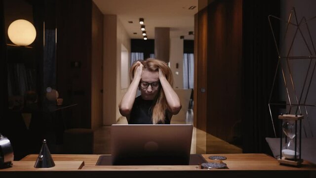 A woman in a home office works at a laptop, grabs her head, receives bad news, closes the laptop lid, is very worried, falling stock prices. Remote work. Freelance.Tired. High quality 4k footage