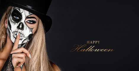Beautiful model in Halloween makeup on black background. Sexy woman in top hat and skull makeup. Halloween makeup concept.