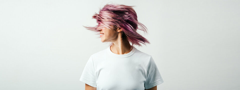 Positive and joyful plus size model with white blank t-shirt and pink hear, empty grunge wall background. Shaking her colored hair