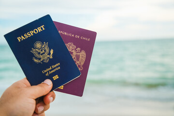 a hand holding two passport a red and a blue one on a beach